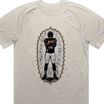A light beige heathered t-shirt featuring a central graphic of a player in a uniform framed by a gold ornate border.